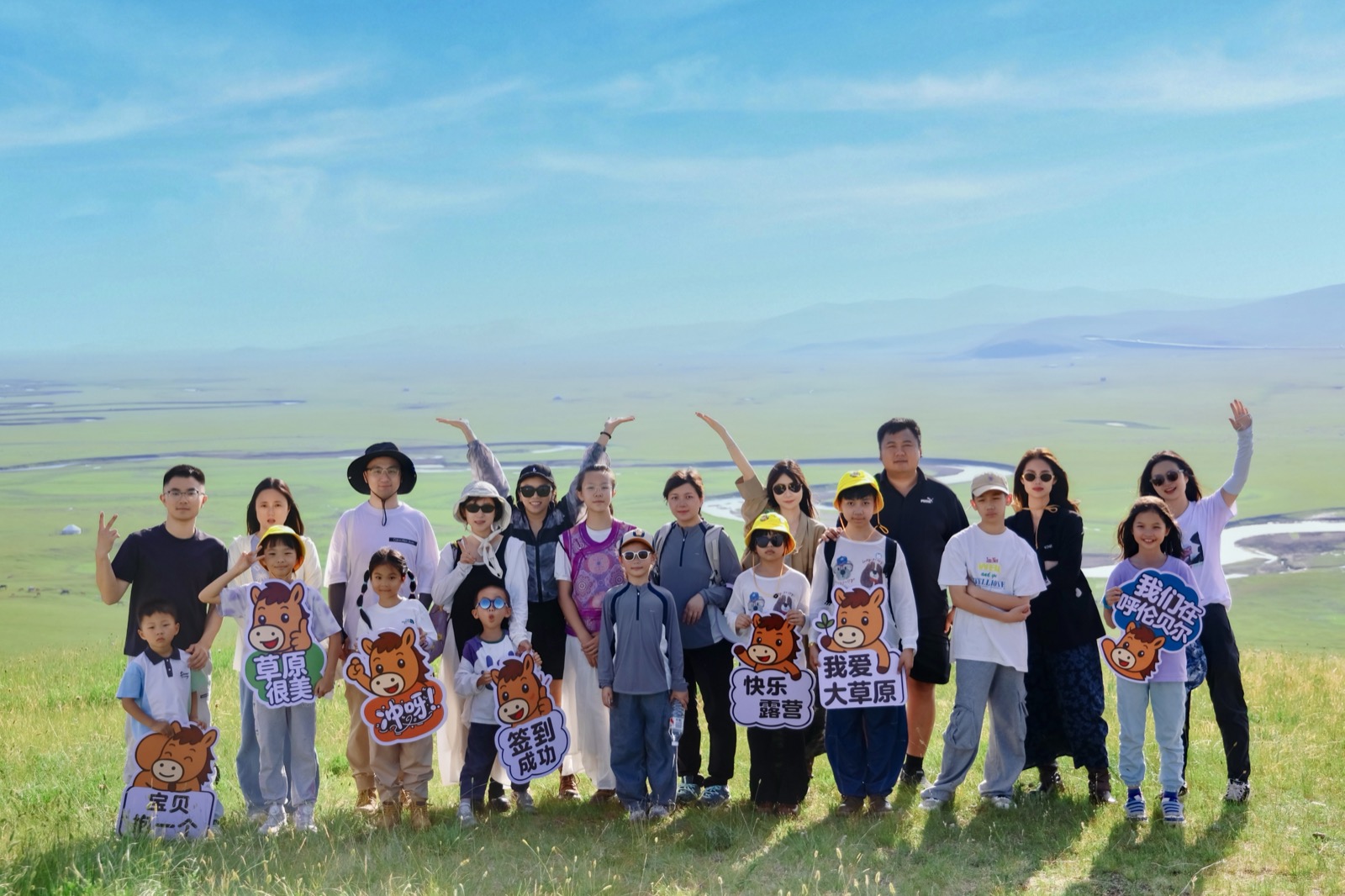 小蒙马夏令营亲子家庭在呼伦贝尔草原上合影，手持小蒙马标志牌